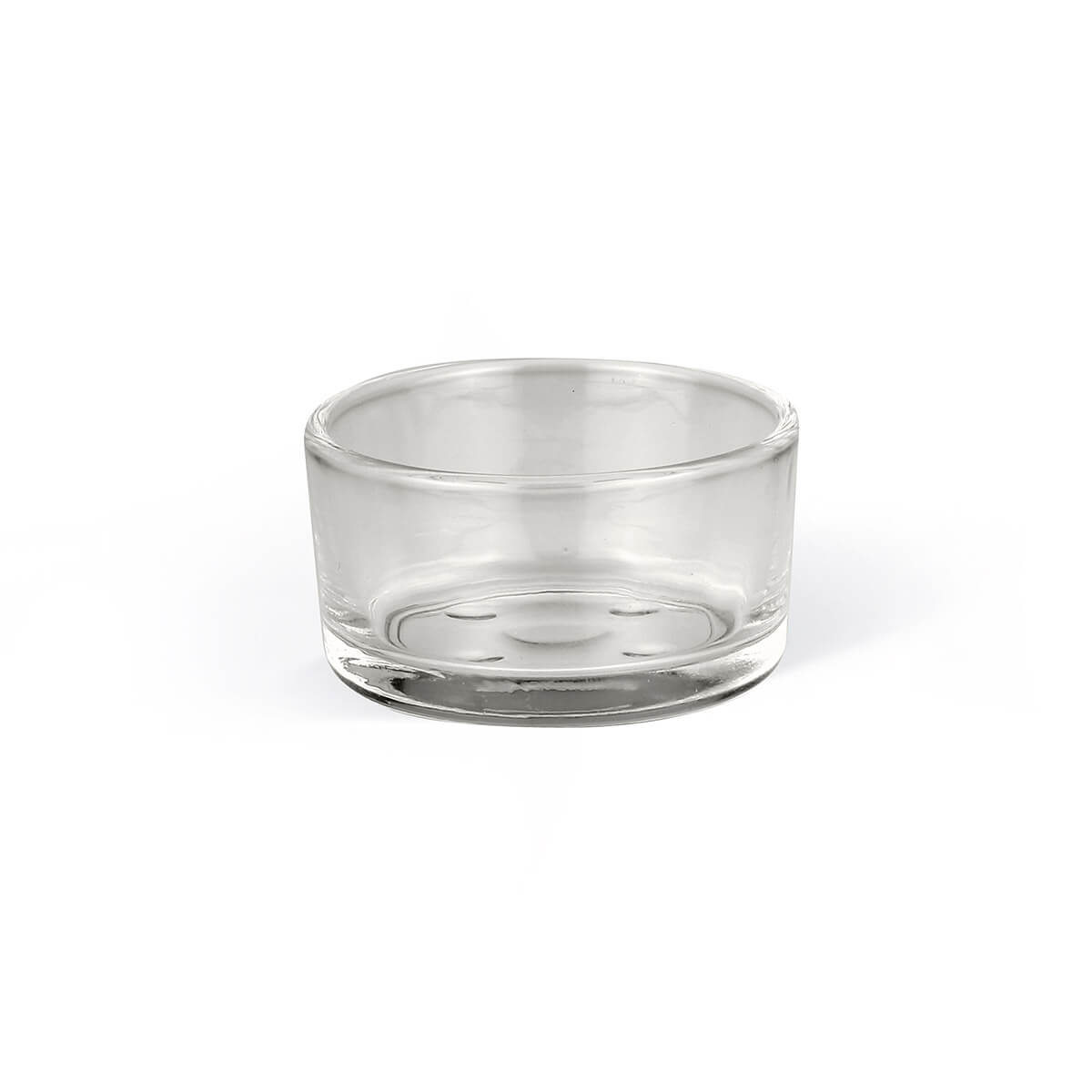 A small, round, transparent glass container, presumably a tea light holder or bowl, against a pure white background. Smooth surface, thickened base with three raised dots for stability. Gentle reflections emphasise the shape.