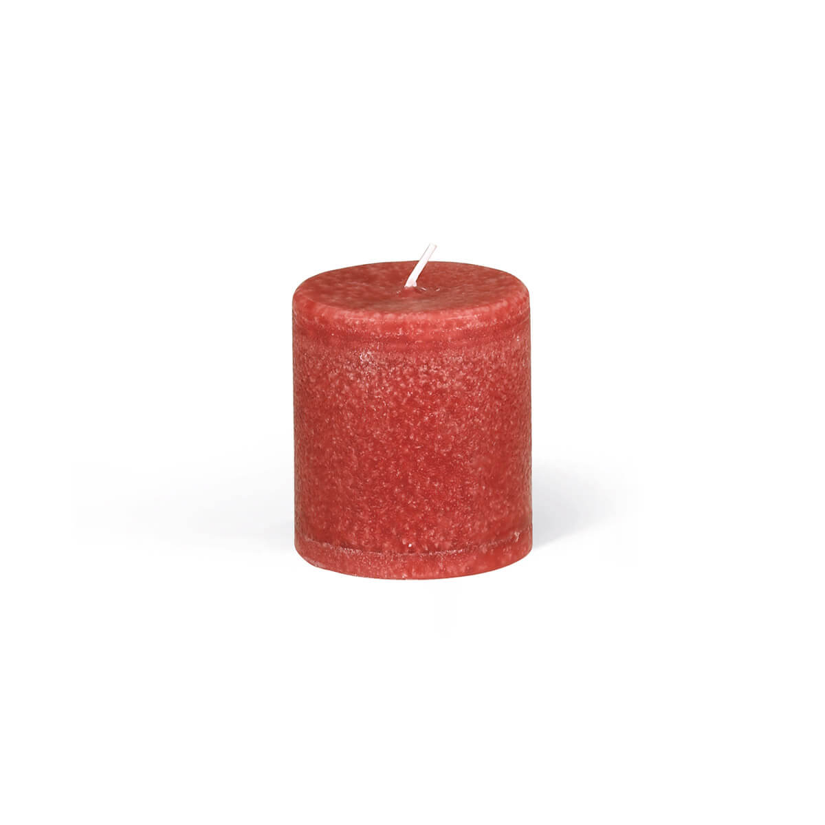 Gros plan sur une bougie cylindrique dans une teinte rouge chaleureuse, avec une surface légèrement irrégulière et texturée. La mèche est centrée sur le dessus plat. La lumière projette une ombre subtile sous la bougie.
