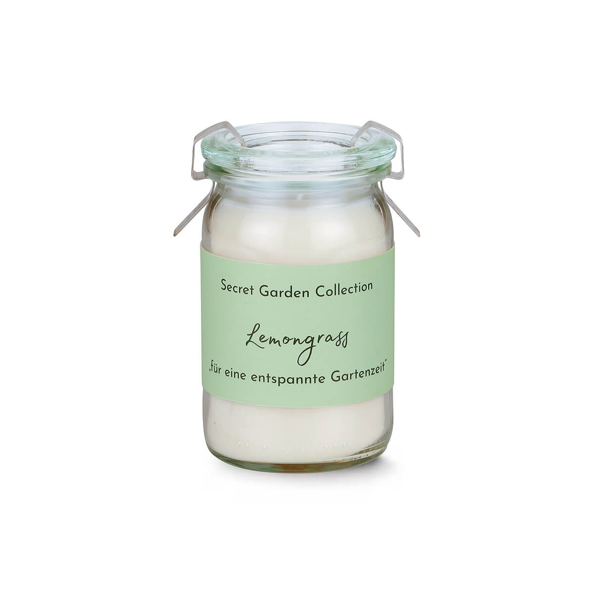 Kleines, klares Glasgefäß mit geöffnetem Metallbügelverschluss, gefüllt mit weißem Wachs. Hellgrüne Banderole mit Aufschrift „Secret Garden Collection Lemongrass für eine entspannte Gartenzeit“. Mittig vor weißem Hintergrund.