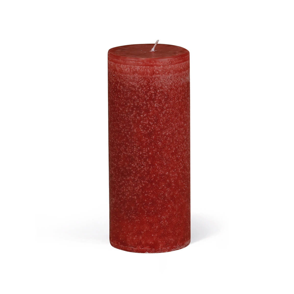 Une bougie cylindrique rouge repose sur un fond blanc. La bougie présente une surface légèrement rugueuse et une mèche blanche courte au centre. La lumière projette une ombre douce sur le fond.