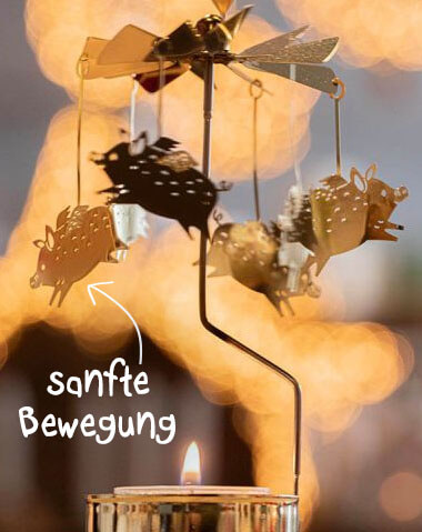 Eine goldfarbene Metall-Weihnachtspyramide mit brennender Kerze setzt durch aufsteigende Wärme einen Rotor in Bewegung. Detaillierte Schweinefiguren in Gold und Schwarz mit Punkten drehen sich sanft. Warme, unscharfe Lichter im Hintergrund.