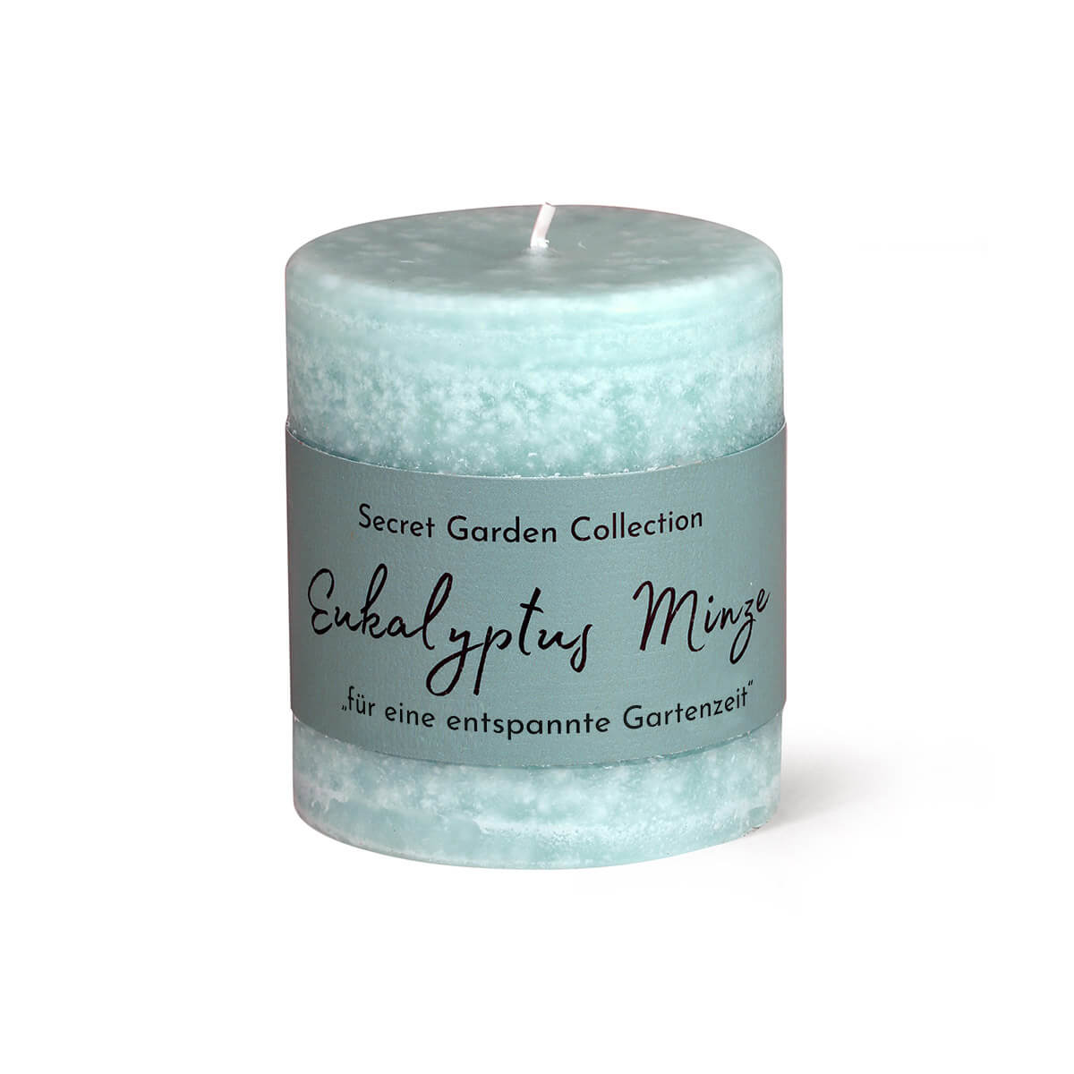 Candela cilindrica azzurra su sfondo bianco, con superficie leggermente ruvida e stoppino bianco. Etichetta blu scuro: "Secret Garden Collection", "Eucalipto e menta", "per rilassanti momenti in giardino".