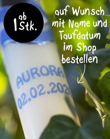 Close-up of a christening candle with blue lettering reading "Aurora" and the christening date "02.02.2021" on a white background. At the top, a black circle with "from 1 pc.". Green leaves in the background. Lettering available to order in the shop.